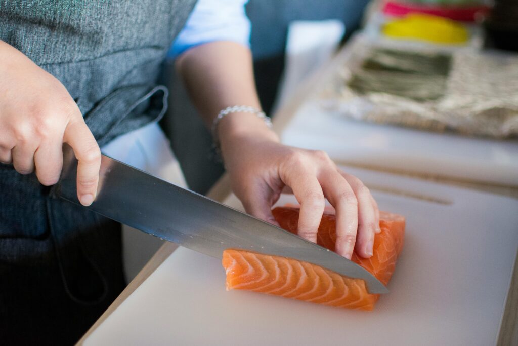 Close-up of a chef's hands slicing fresh salmon for sushi on a cutting board indoors.