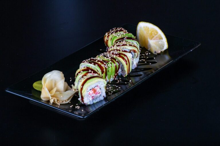 Mouthwatering sushi roll topped with avocado and sesame, garnished with ginger and lemon.