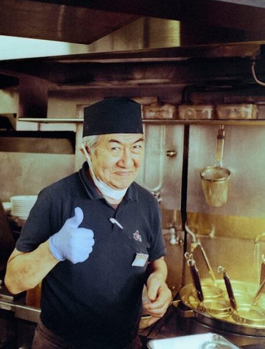Cheerful chef giving thumbs up in a traditional Japanese ramen restaurant kitchen.